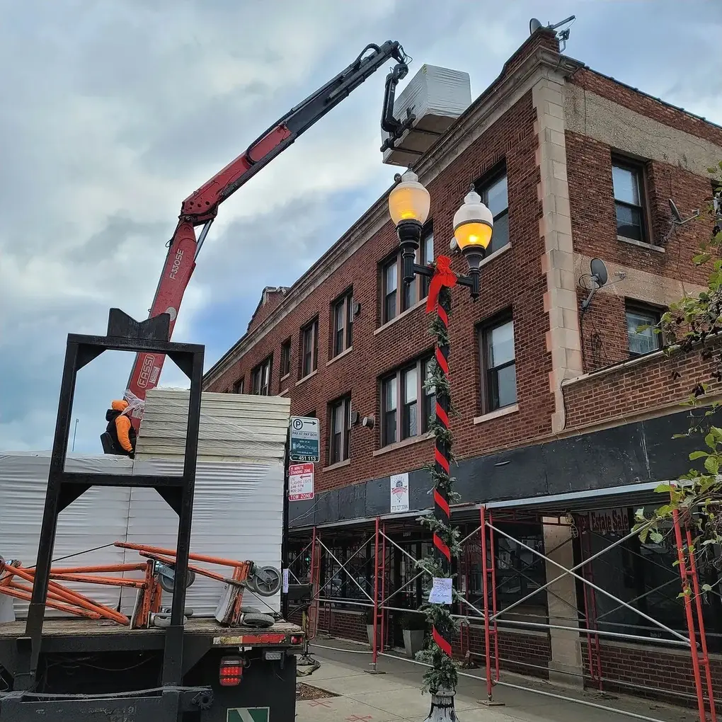 Crane lifting packaged roofing materials to the top of a multi-story brick commercial building
